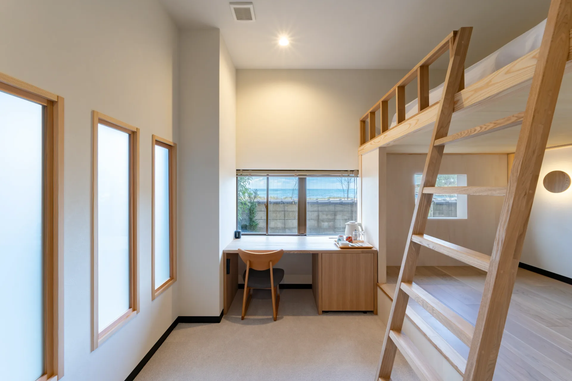Standard room 101, a lofted bed and wooden desk with a glimpse of the sea through the window